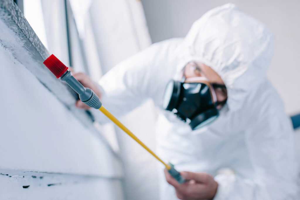 A man in a white protective suit and mask is painting a wall with a roller, ensuring safety while working